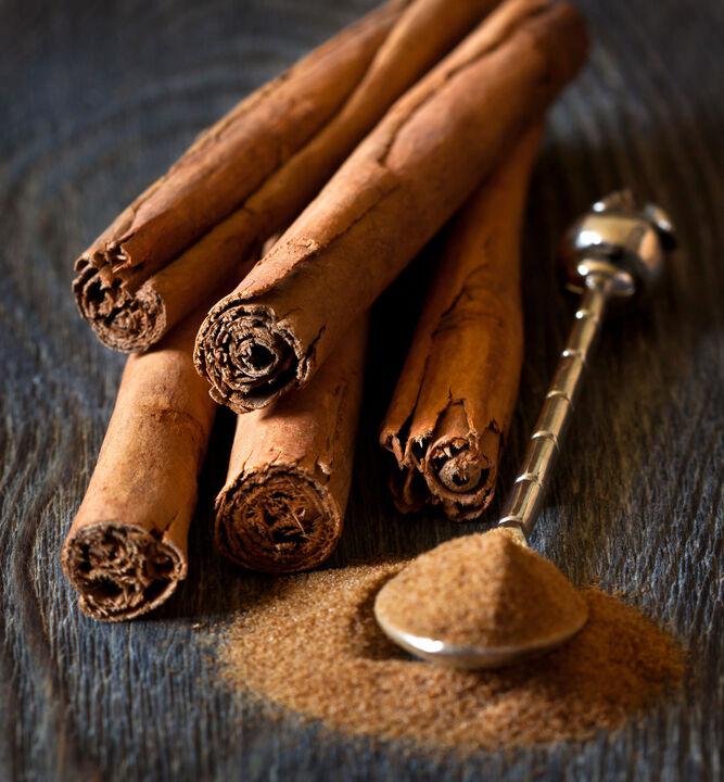 Close-up of Ceylon cinnamon resting on a wooden tabletop. Next to it on the right is a fancy spoon sitting on top of a small mound of ground Ceylon cinnamon. The spoon is holding some of the cinnamon as well.